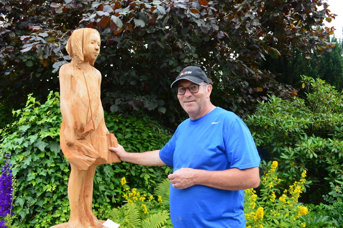 Ein Mann steht neben einer Holzfigur und lächelt.